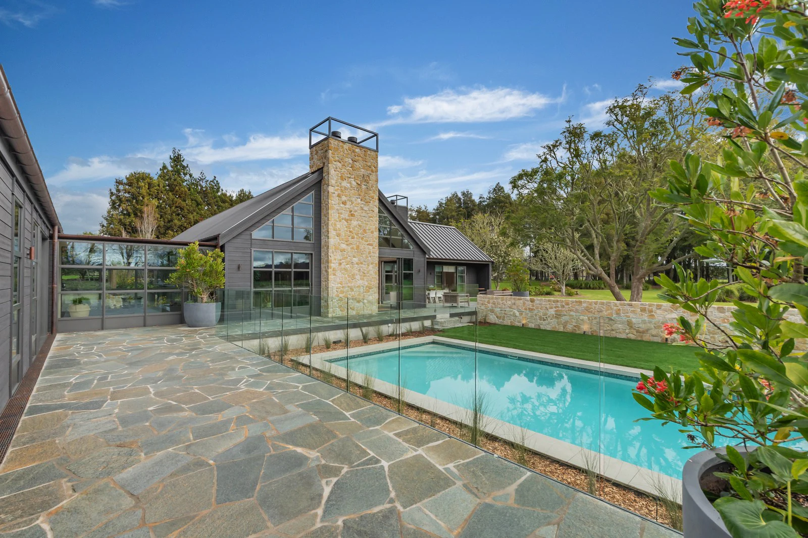 The Clevedon home's pool and stone chimney, seen across a flagstone terrace under a clear sky