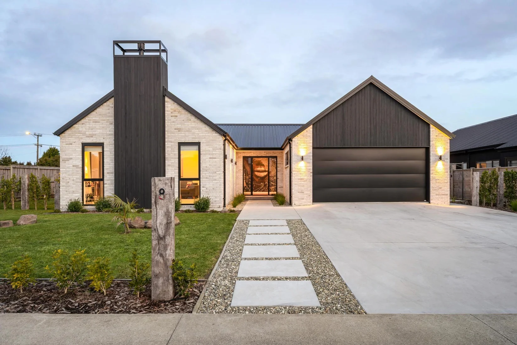 A dusk-lit brick and dark-timber gable home, warmly lit from within